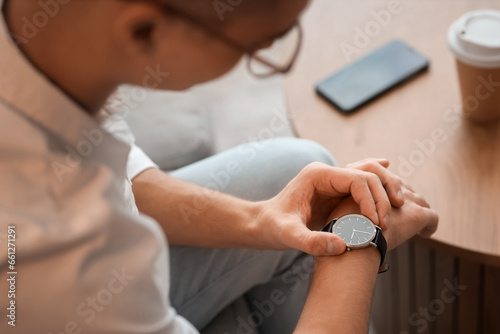 Young man looking at wristwatch in room  closeup