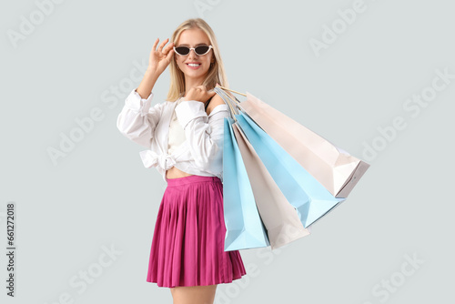 Beautiful young woman in sunglasses with shopping bags on grey background