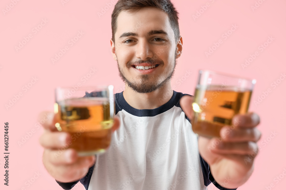Young man with glasses of juice on pink background