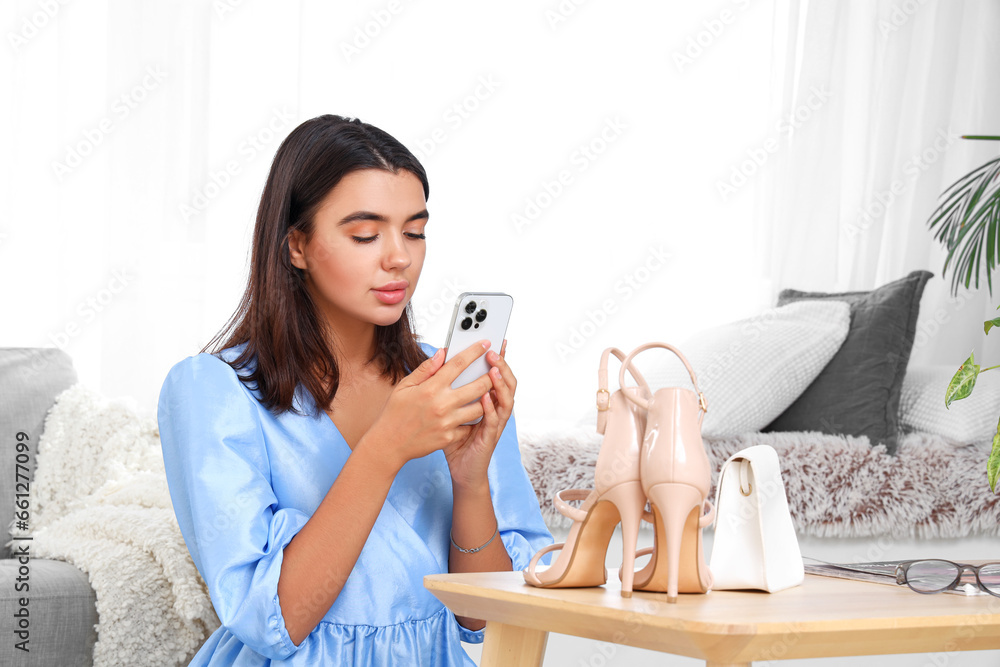 Young woman with mobile phone taking picture of bag and heels at home Young woman with mobile phone taking picture of bag and heels at home