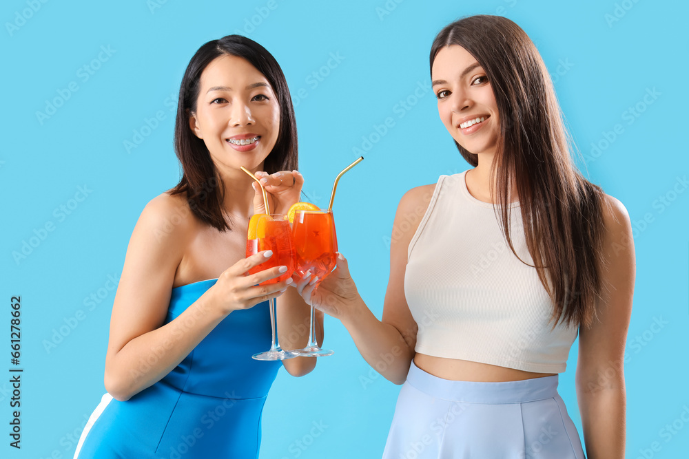Beautiful young women with glasses of tasty aperol spritz cocktail on blue background Beautiful young women with glasses of tasty aperol spritz cocktail on blue background