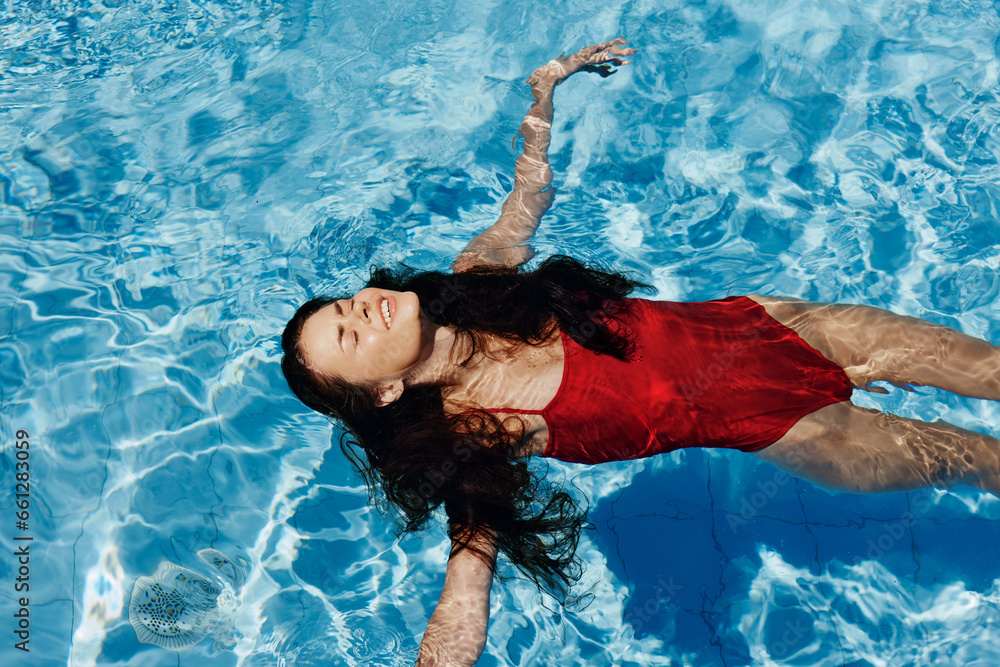 Happy woman swimming in the pool in red swimsuit with loose long hair relaxed in the sunshine, skin protection with sunscreen, concept of relaxing on vacation in tropical climate, lifestyle.