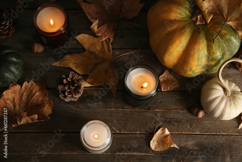 Burning candles with autumn leaves, pumpkin and pine cones on wooden background