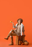 Beautiful young woman with pumpkins and wooden box on orange background