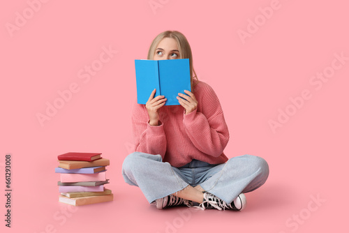 Beautiful young woman with many books sitting on pink background