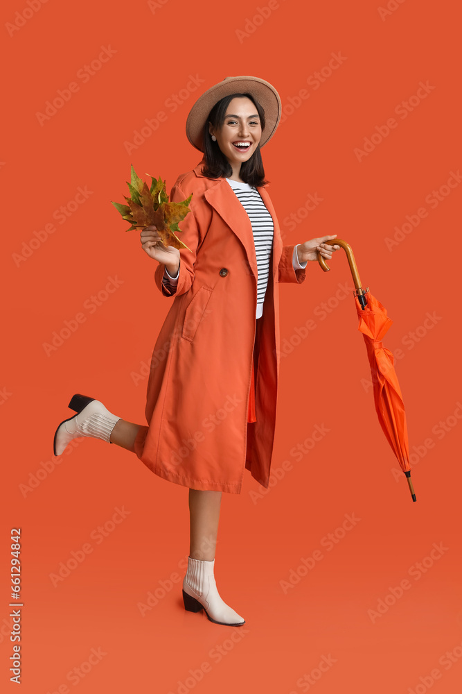Beautiful young woman with autumn leaves and umbrella on red background