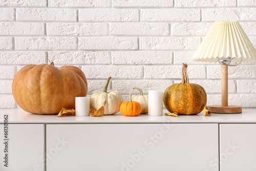 Cabinet with pumpkins, lamp and candles near white brick wall