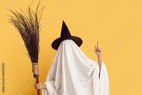 Woman in Halloween costume of ghost with witch broom pointing at something on color background