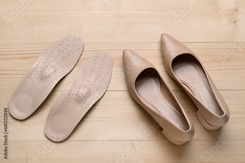 Pair of orthopedic insoles and stylish high heeled shoes on wooden background