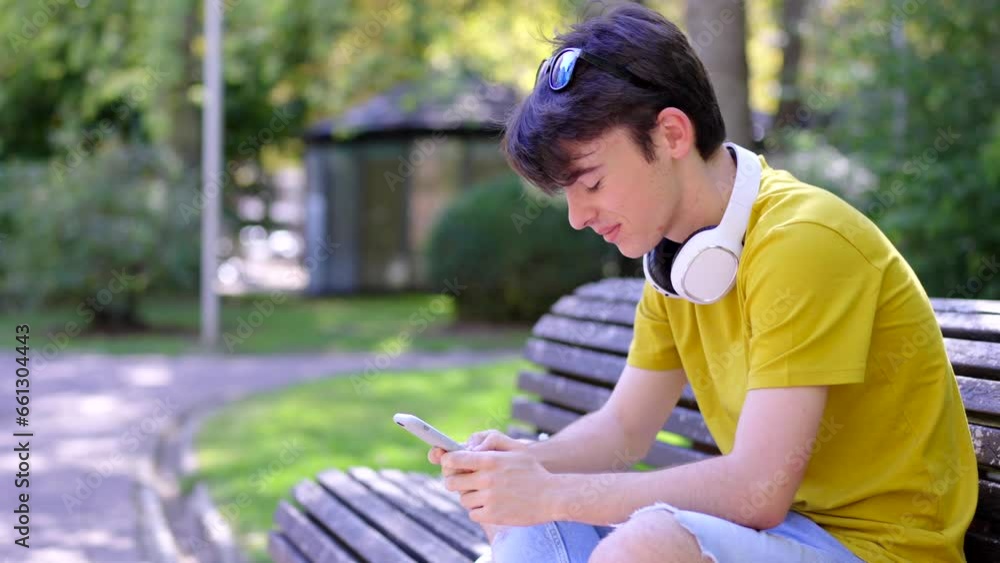 Teenager boy using phone sitting on a bench in a park Teenager boy using phone sitting on a bench in a park
