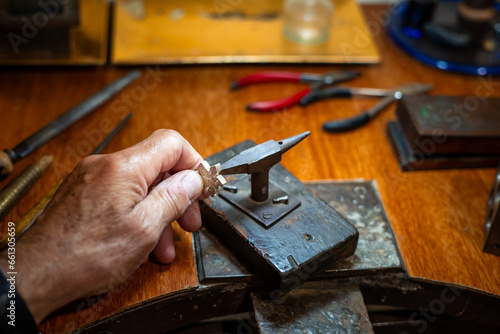 Bild auf Leinwand Goldsmith creating and repairing in his crafting gold jewelry workshop with an anvil