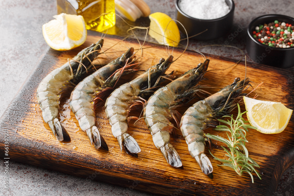 Raw unpeeled black tiger prawns, shrimps with lemon, herbs and spices closeup on the wooden board on a table. Horizontal Raw unpeeled black tiger prawns, shrimps with lemon, herbs and spices closeup on the wooden board on a table. Horizontal