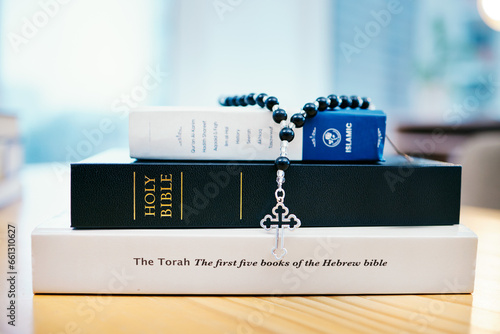 Books, stack and closeup on table for faith, Abrahamic religion or rosary with crucifix for study in home. Knowledge, holy spirit and education with cross for Jesus, Muhammad or Moses with solidarity photo