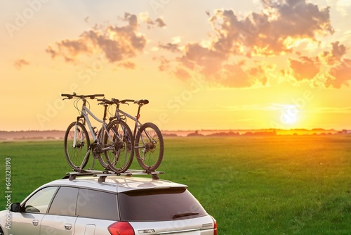 Fototapeta Naklejka Na Ścianę i Meble -  Mounted sport mountain bicycle silhouette on the car roof with evening sunlight rays background. Concept of safe items transportation using a car with roof rack
