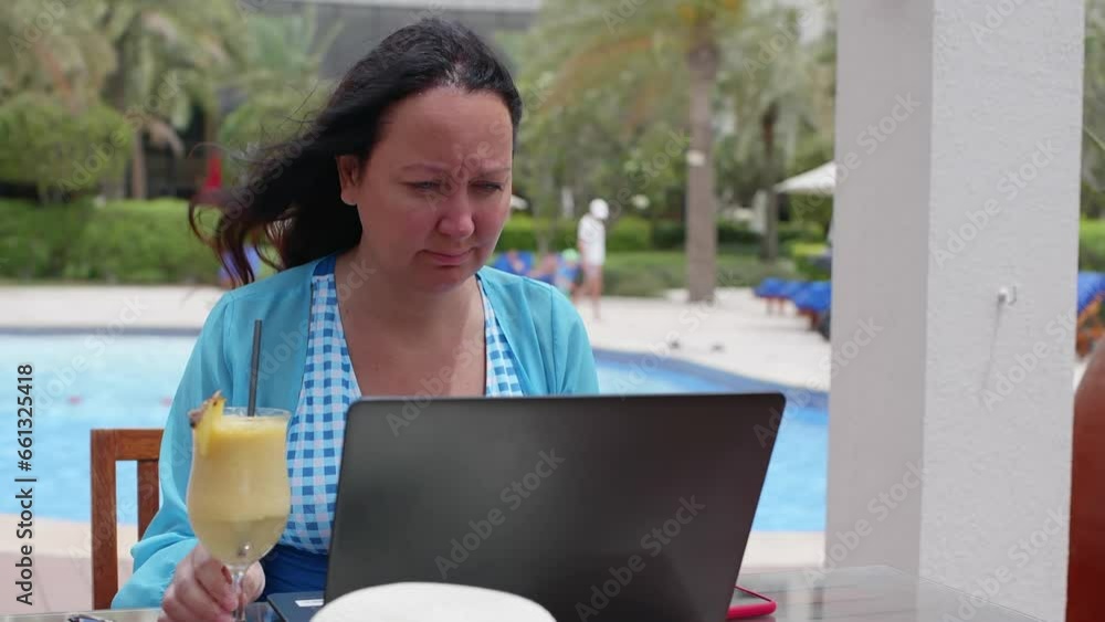 Portrait of frown woman having problems at work looking at laptop on resort sitting in cafe near pool. Brunette female tourist freelancer workaholic working on computer drinking cocktail on vacation. Portrait of frown woman having problems at work looking at laptop on resort sitting in cafe near pool. Brunette female tourist freelancer workaholic working on computer drinking cocktail on vacation.