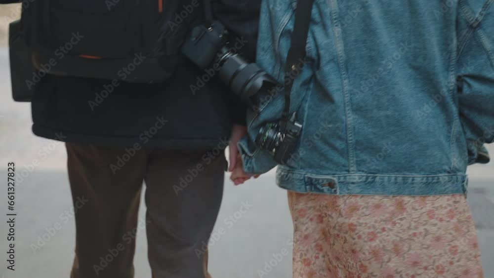 Couple holding hands, cameras on shoulders, exploring a urban setting Couple holding hands, cameras on shoulders, exploring a urban setting