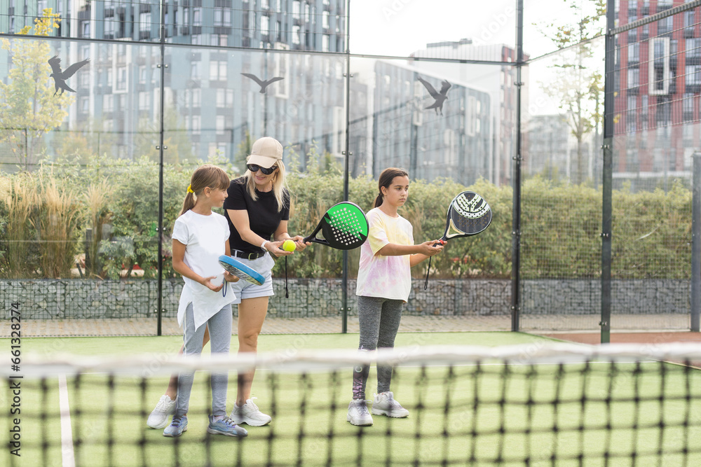 Cheerful coach teaching child to play tennis while both standing on tennis court