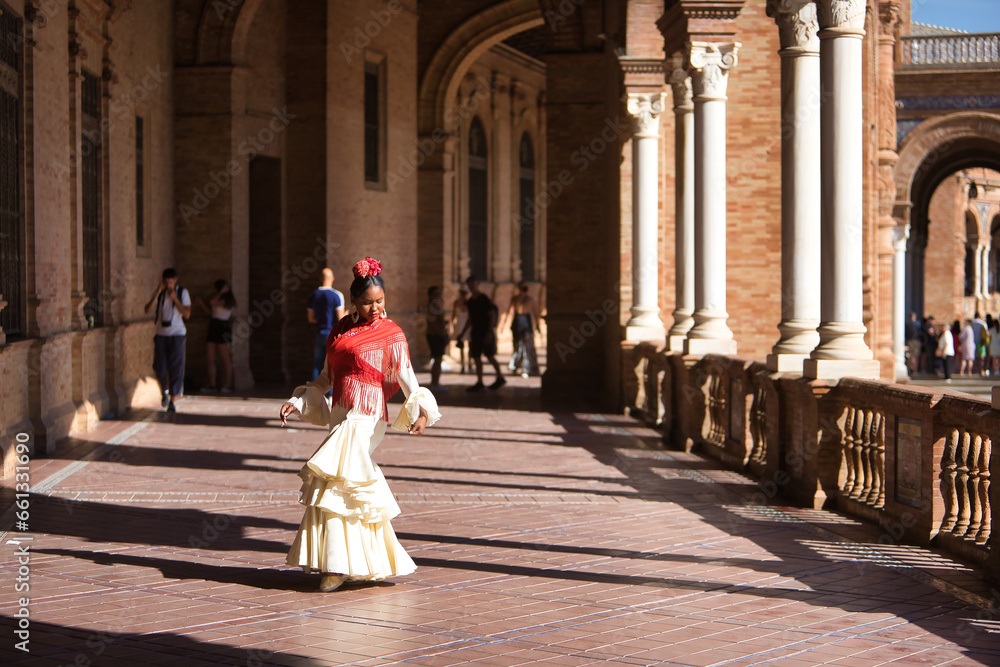 Young black and South American woman in a beige gypsy flamenco suit, posing in a beautiful square in the city of Seville in Spain. Concept dance, folklore, flamenco, art.
