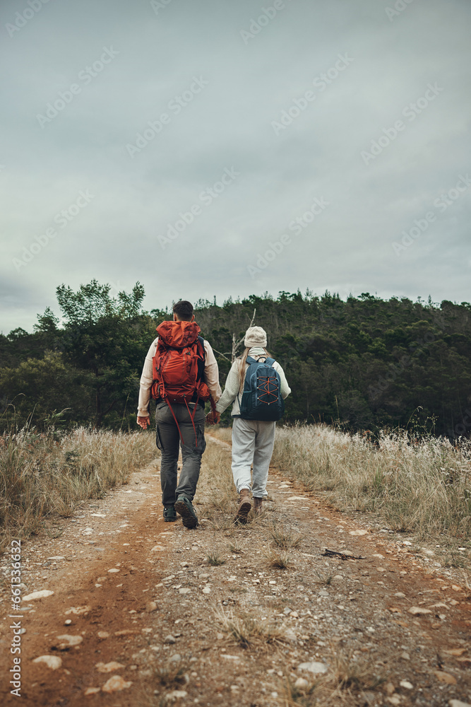 Couple back view, hiking and holding hands in nature with travel, mountain and backpacking in wilderness and explore outdoor. People on adventure, holiday date and environment with trekking path