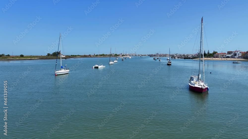 Drone shot flying low over the water surface with sailboats anchored on either side. Drone shot flying low over the water surface with sailboats anchored on either side.