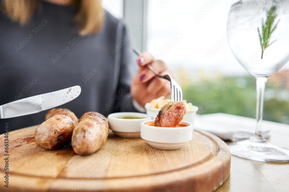 A piece of sausage is dipped in sauce. Lunch in a restaurant, a woman
