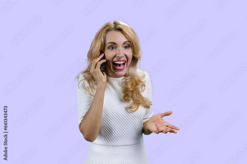 Emotional happy mature blonde woman talking on the phone. Isolated on purple. Emotional happy mature blonde woman talking on the phone. Isolated on purple.