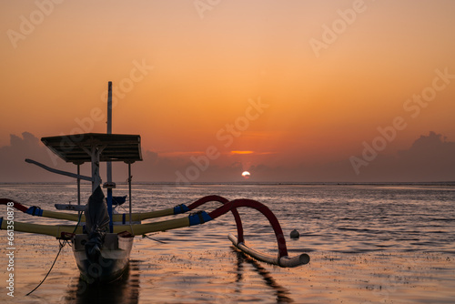 Levé du soleil avec une pirogue à balancier indonésienne sur la plage de Karang à Bali. 