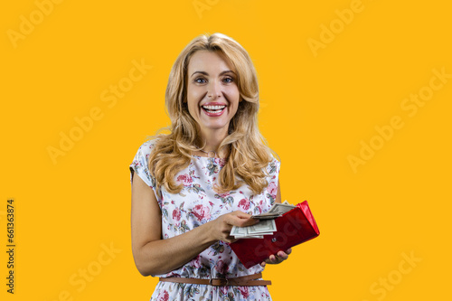 Portrait of happy smiling blonde woman taking money from her wallet. Isolated on yellow. photo