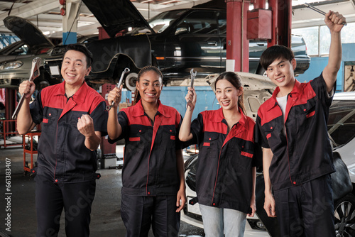 Multiracial professional mechanic workers team after work celebrating automotive repair jobs success, hand raises with fixing tools with cheerful smiles and look at camera at a service car garage.