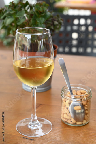 Verre de vin blanc avec un bocal de cacahuètes posés sur une table en gros plan