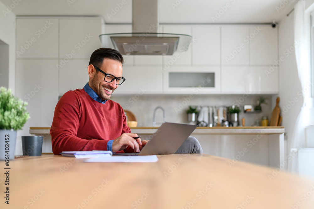 Smiling businessman with note pad and documents on desk working over laptop in home office Smiling businessman with note pad and documents on desk working over laptop in home office