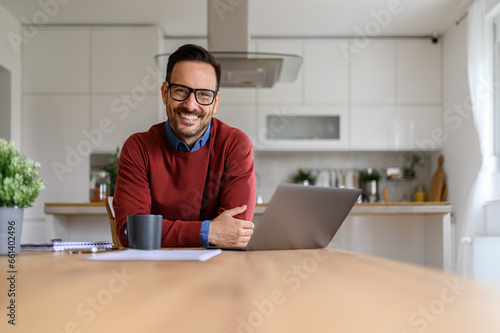 Portrait of confident businessman with laptop on desk looking at camera while working from home