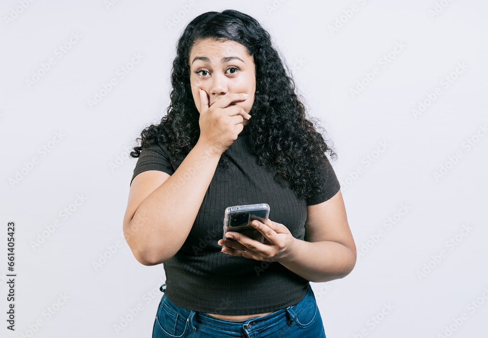 Surprised young woman covering mouth holding phone isolated. Astonished young girl holding phone and covering mouth isolated Surprised young woman covering mouth holding phone isolated. Astonished young girl holding phone and covering mouth isolated