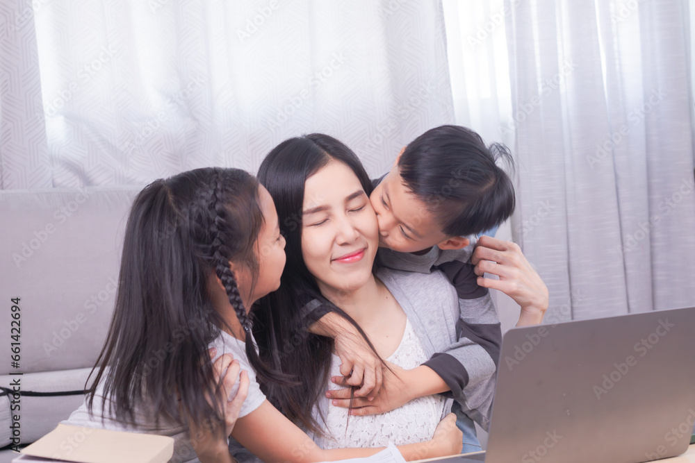 Happy single mom with children playing together bonding relationship at home, Asian freelancer woman working at home using modern technology laptop, kids sibling run to hug mother from behind and kiss Happy single mom with children playing together bonding relationship at home, Asian freelancer woman working at home using modern technology laptop, kids sibling run to hug mother from behind and kiss