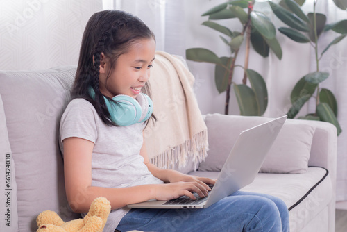Asian preteen schoolgirl doing homework on digital modern technology laptop, kid elementary girl using gadget study with distance homeschool online learning stay at home, education for student work