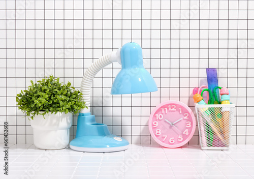 School and workplace. Blue lamp, pink clock and stationery. A green plant in a white pot.