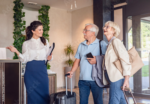 A senior couple is arriving at the hotel with luggage, and a smiling hotel representative is welcoming them