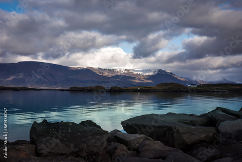 Landscape with Mount Esja and Atlantic ocean in Reykjavik, Iceland. Shining water, cloudy sky, big rocks in foreground. 