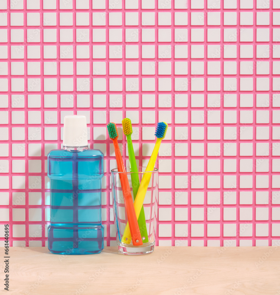 Blue mouthwash, brightly colored toothbrushes in a glass. Copy space for text. Set for dental hygiene.