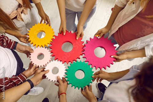 Group of school, college or university students working on project all together. Team of young people holding colorful green, pink, red, yellow gear cog wheels. Top view. Education, teamwork concept