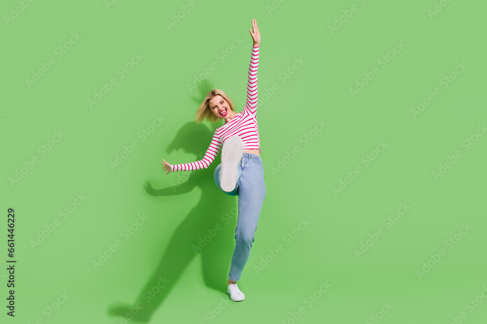 Full length photo of cheerful shiny girl dressed striped shirt walking having fun discotheque empty space isolated green color background