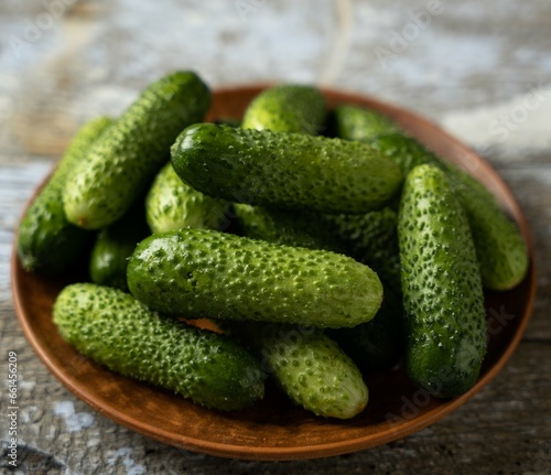 Green cucumbers on a plate, old wooden background, square format, top view