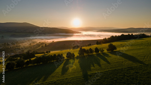 Sunrise in czech mountains with foggy valley with village and meadows. 