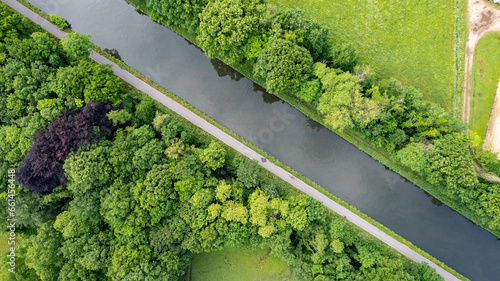 An exquisite top-down aerial view of a serene river or canal winding its way through lush green meadows and the tranquil embrace of forested trees. Aerial River Between Trees and Meadows. High quality