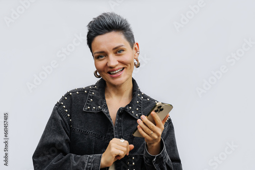 Portrait of cheerful girl a short gray hair using smartphone. Woman in fashion jean jacket on a white background. Trend women's haircut hairstyle.