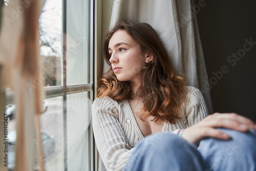 Dreamy teen woman looking at the window while spending time at home alone