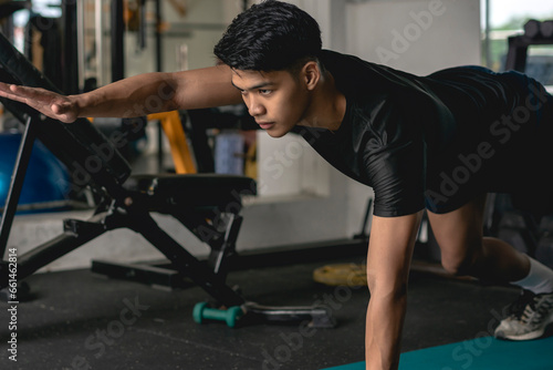 Bild auf Leinwand A young handsome asian man executes a prone two point bridge exercise on the mat at the gym