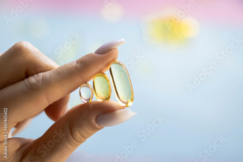 Young female hands are holding yellow omega 3 gel capsule close-up. Fish oil supplement. The concept of health, vitamins, and medicine. Omega 3 fish oil capsules, vitamin E