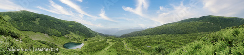 Lake on green mountains valley. Blue sky with white clouds. Rewilding and recreation concept.