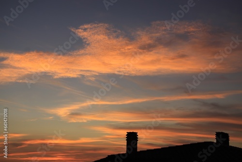 a sunset with a few clouds in the sky and a building with a chimney in the foreground